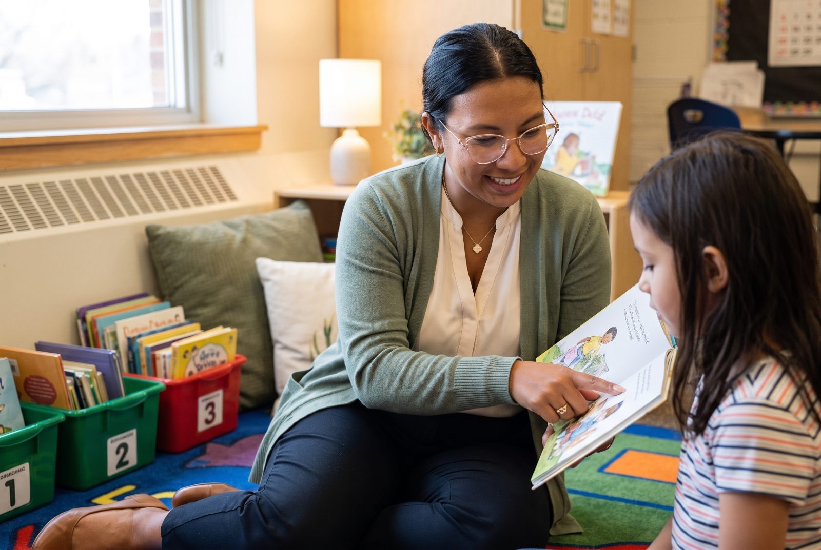 Janessa reading one-on-one with a student on the classroom rug